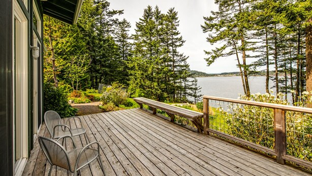 A wooden deck with a bench and chairs, overlooking a lake with trees and a distant shoreline. - Orcas Island, Casa Verde #269 (Eastsound)
