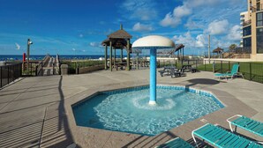 A pool area with a water fountain, lounge chairs, and a gazebo.