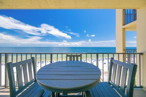 Een balkon met een tafel en stoelen, uitzicht op een strand met parasols en mensen.