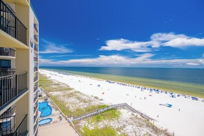 Uitzicht op het strand vanaf een balkon van een hotel, met een zwembad en strandparasols.