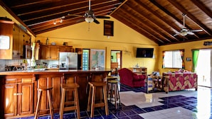 Una cocina amplia con armarios de madera, una isla central con taburetes, un ventilador de techo y un comedor con una silla y una mesa rojos.