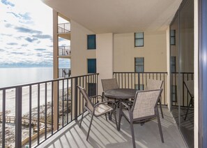 En balkon med et rundt bord og stole, der giver udsigt over en strand og havet.