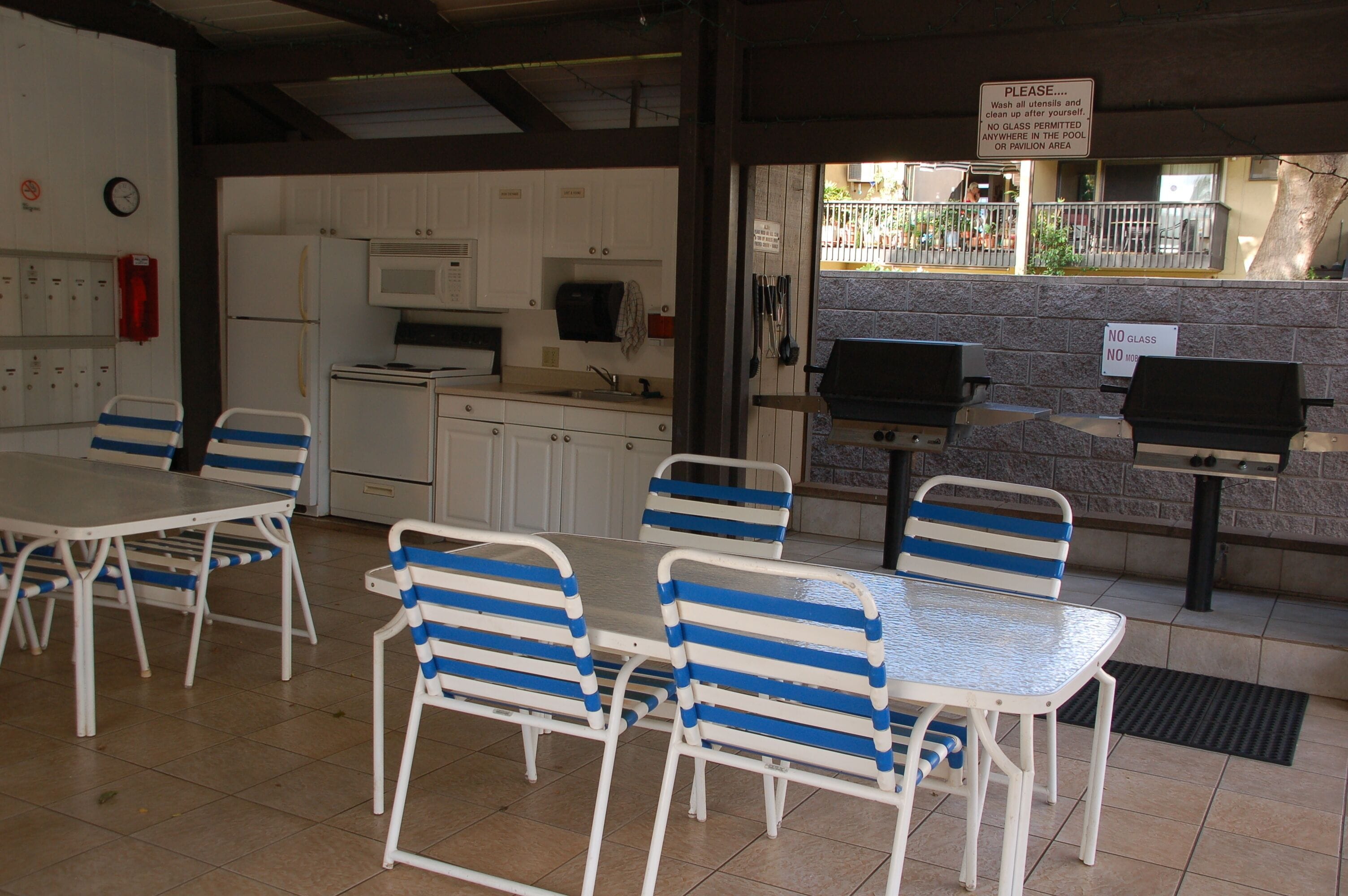 A poolside area with a dining setup including tables and chairs, a grill, and a view of the pool.