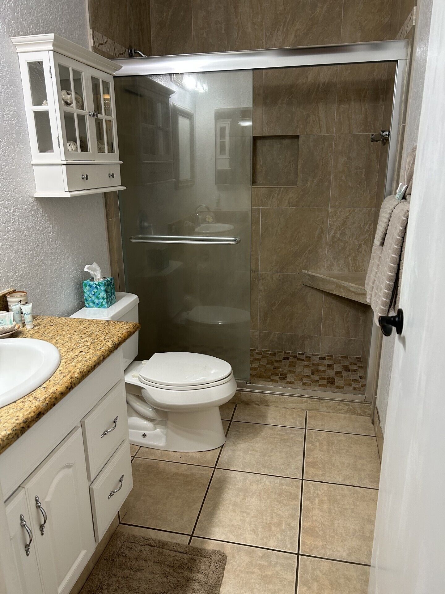 A bathroom with a toilet, sink, cabinet, and shower area.