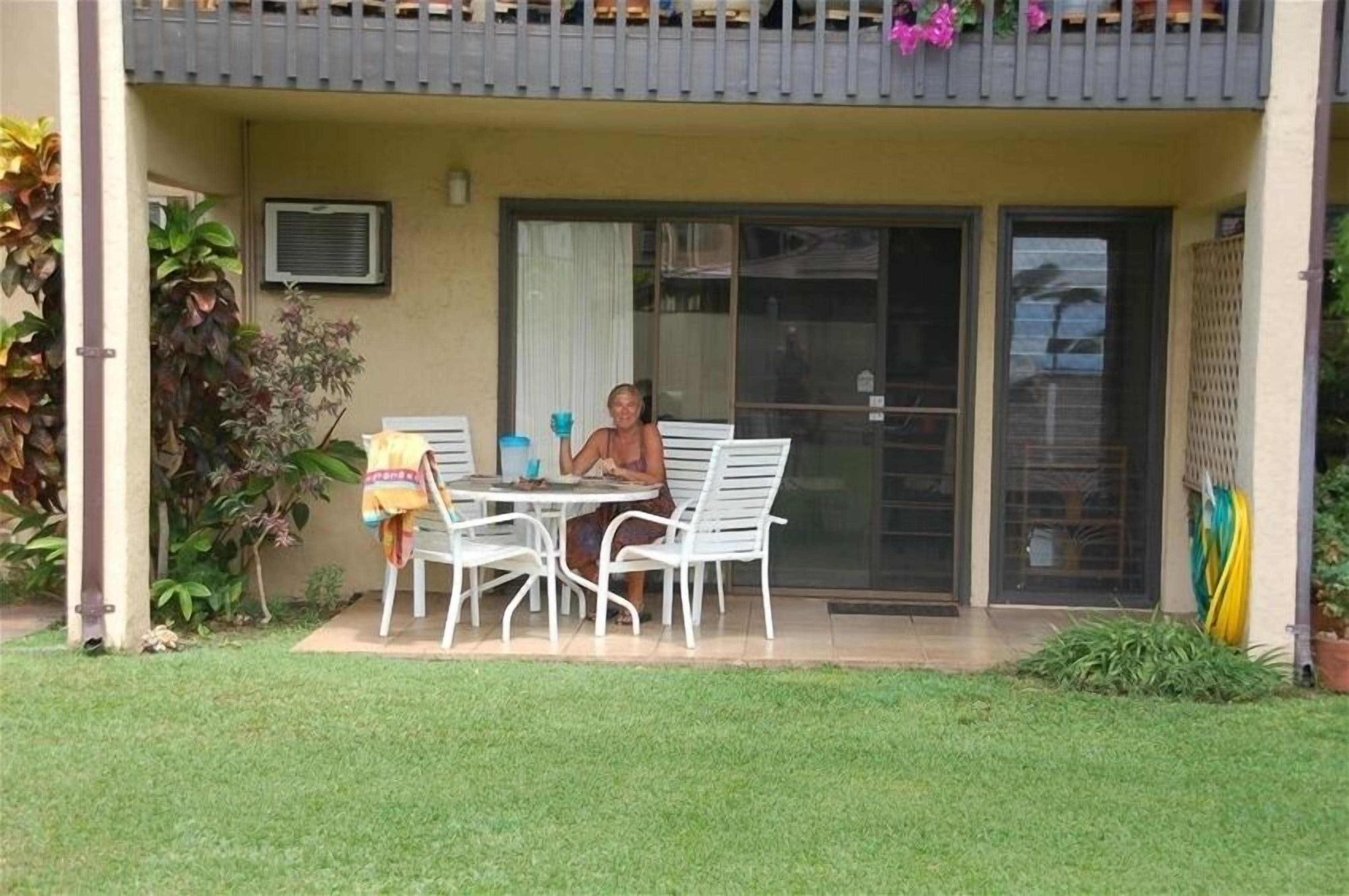 Une terrasse avec une table et des chaises, une personne assise, et un balcon agrémenté de plantes.