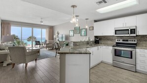 A modern kitchen with a central island, stainless steel appliances, and a large window overlooking the ocean.