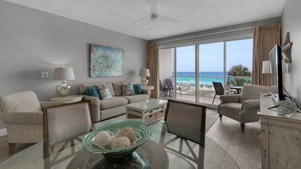 A spacious living room with a large window offering a view of the ocean, a ceiling fan, and a modern fireplace.
