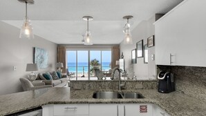 A modern kitchen with granite countertops, stainless steel appliances, and a large window overlooking the ocean.
