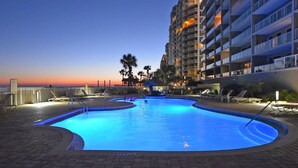 A swimming pool with a sunset view, surrounded by lounge chairs and a multi-story building.