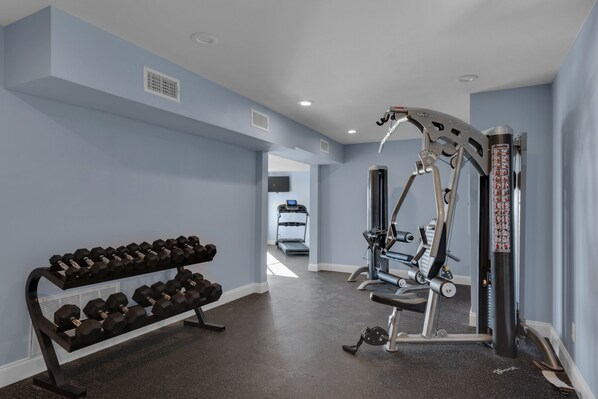 Un gimnasio con banco para mancuernas, cinta de correr y máquina de pesas.