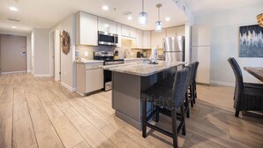 Una cocina moderna con una isla central, electrodomésticos de acero inoxidable y un comedor con sillas de mimbre.