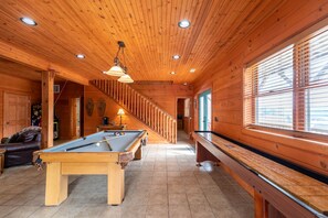Interior de madeira com mesa de bilhar, mesa de sinuca e uma escada.