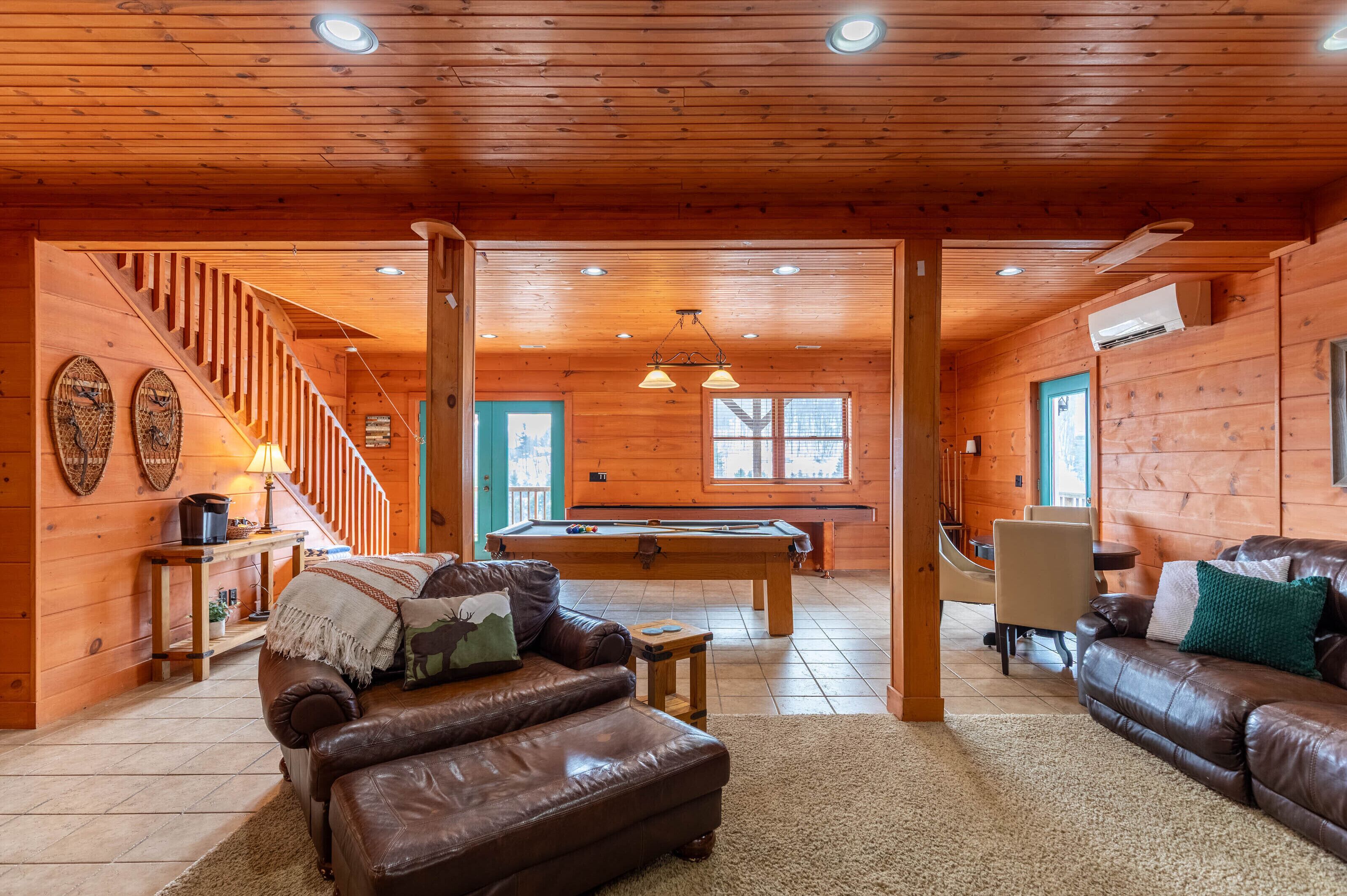 L’intérieur d’un chalet en bois comprend une table de billard, des canapés en cuir, un escalier et une table de jeu de billard.