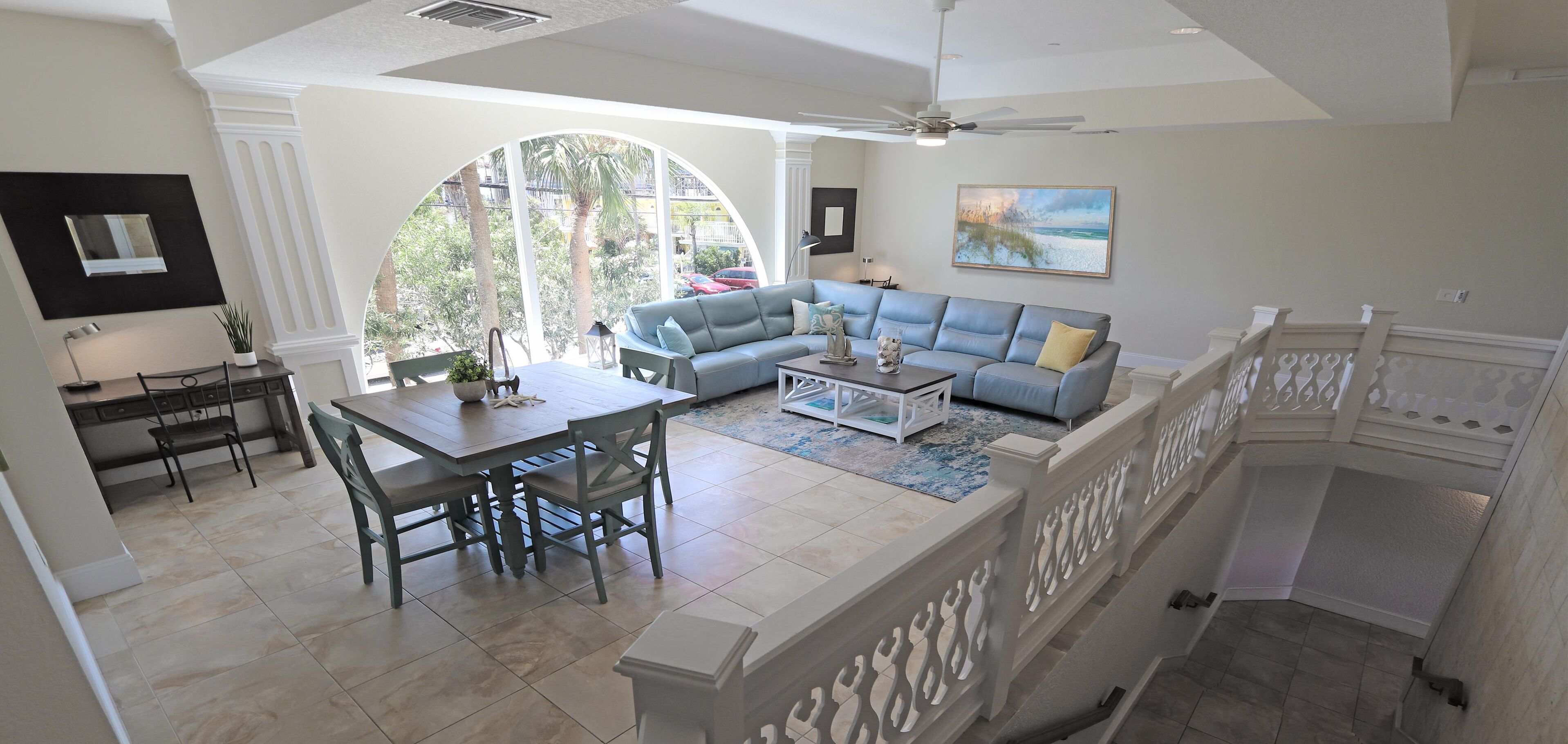 A spacious living area with a large window, a grey sofa, a coffee table, and a dining table with chairs.