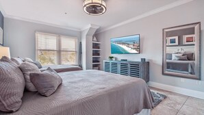 Un dormitorio con una cama grande, un televisor montado en la pared y una ventana con persianas.