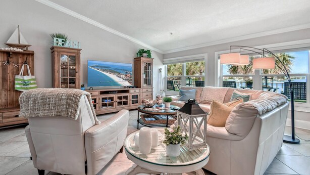Una sala de estar con un televisor grande, un sofá, una mesa de centro de vidrio y vista al mar.