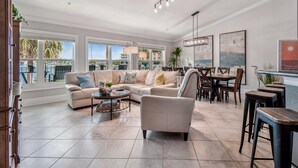 Un salón espacioso con un amplio sofá seccional color beige, una mesa de centro redonda y un comedor con sillas y mesa de madera.