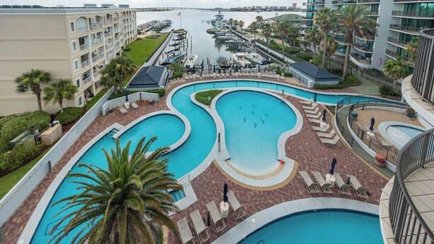 A large, multi-lane swimming pool with a curved design, surrounded by lounge chairs and palm trees. - Bay Breezes, Perfect Ease Lighthouse on the Bay 2513 (Orange Beach)