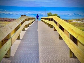 En träpromenad som leder till en strand, och en person går mot vattnet.