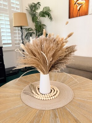Un jarrón blanco con plumas de pampa seca sobre una mesa redonda con un mantel tejido.