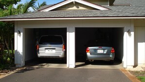 A garage with two cars parked inside, a clear sky, and palm trees in the background.