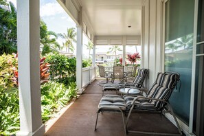 A covered outdoor seating area with chairs and tables, surrounded by lush greenery and palm trees.