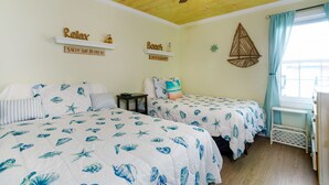 A room with two beds, a ceiling fan, and a window with curtains.