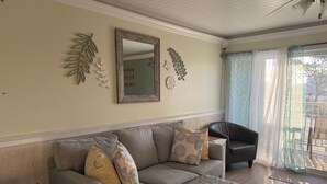A living room with a sofa, ottoman, and a chair. There are decorative wall hangings and a mirror.