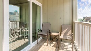 A balcony with two chairs and a small table, a glass door leading to a deck, and a view of buildings in the background.