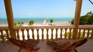 A balcony with two wooden chairs, a view of the beach, and a thatched-roof structure. - Rustic Ocean front Home with POOL-115' of beachfront 250 ft Dock-
GOLD STANDARD (San Pedro)