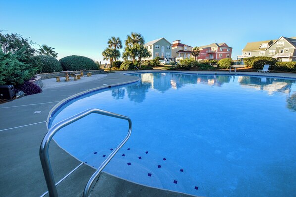 Piscina con una escalera metálica, rodeada de un área ajardinada con bancos y palmeras.
