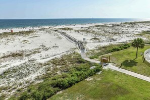 Una spiaggia con una passerella di legno che conduce all'acqua, circondata da dune sabbiose e vegetazione rada.