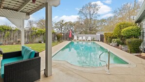 Ein Garten mit Schwimmbecken, einer überdachten Terrasse und einem Holzzaun.