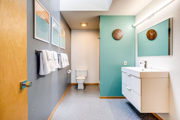 A bathroom with a toilet, sink, and two clocks on the wall.