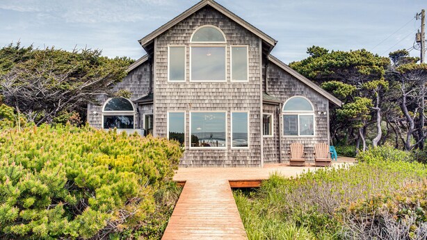 Une maison à deux étages avec une façade en bois, de grandes fenêtres et une terrasse en bois.