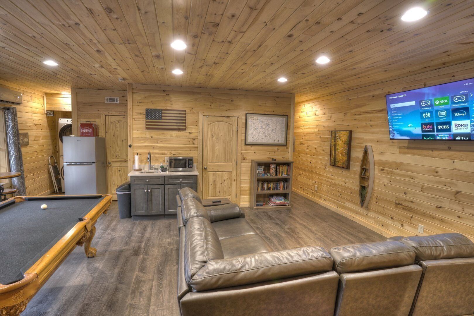 A cozy room with a pool table, a leather sofa, a kitchen area, and a flat-screen TV displaying various channels.