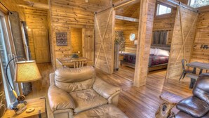 A log cabin interior with a sofa, a dining table, and a bed. - Allure Cabin – Family-Friendly Escape w/ Fire Pit, Creek & Near Helen! (Cleveland)