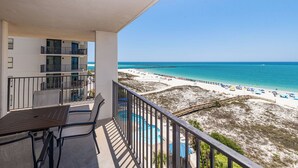 Un balcón con vistas a una playa, una piscina y un edificio de varios pisos.