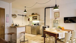 A compact kitchen with a dining area, wooden stools, a table set for two, and a TV mounted on the wall. - Villa PoliFlora is a modern apartment in Monticchiello of Pienza in Tuscany. (Monticchiello)