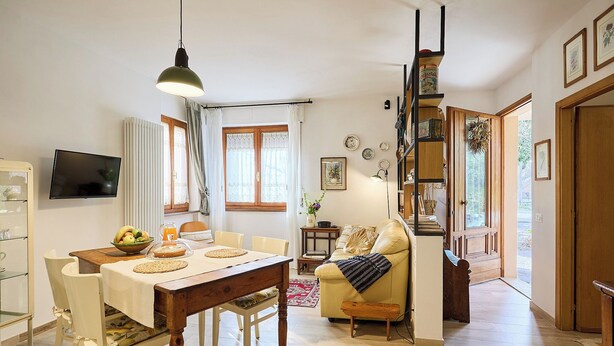 A spacious living area with a wooden dining table, a sofa, and a staircase leading to an upper floor. - Villa PoliFlora is a modern apartment in Monticchiello of Pienza in Tuscany. (Monticchiello)