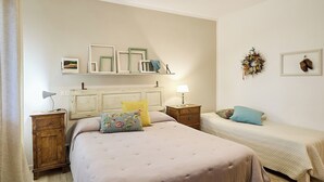 A bedroom with a large bed, two bedside tables, a dresser, and a nightstand. There are wall decorations including a wreath and framed pictures. - Villa PoliFlora is a modern apartment in Monticchiello of Pienza in Tuscany. (Monticchiello)