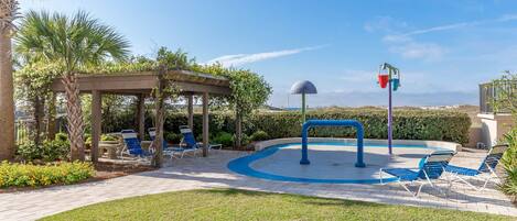 A pool area with lounge chairs, a pergola, and a water feature.