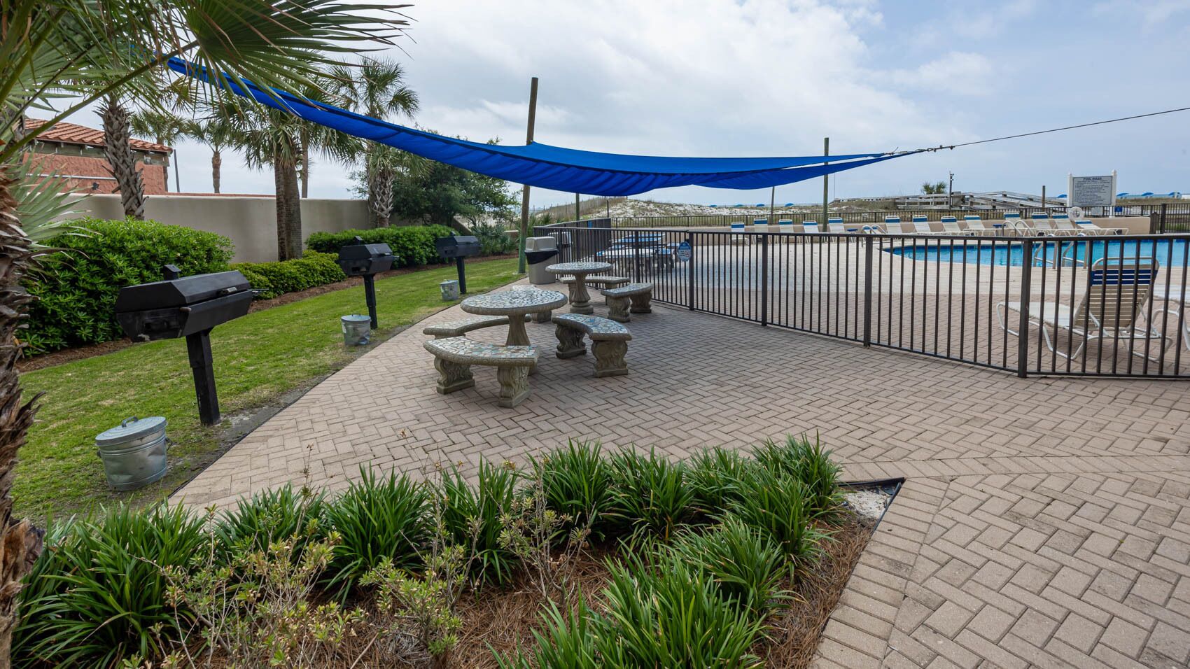 An outdoor patio area with a pool, stone tables, and barbecue grills.