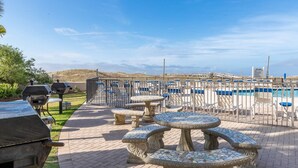 An outdoor patio with stone tables and chairs, a barbecue grill, and a pool area with lounge chairs. - GROUND FLOOR! 3 Bedroom! Phoenix East II - Splash Pad (Orange Beach)