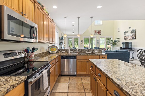 A modern kitchen with granite countertops, stainless steel appliances, wooden cabinets, and pendant lighting.