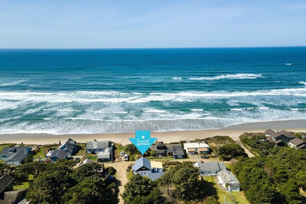 Vue aérienne d’une zone résidentielle côtière, avec des maisons situées près de la plage, un ciel dégagé et l’océan.