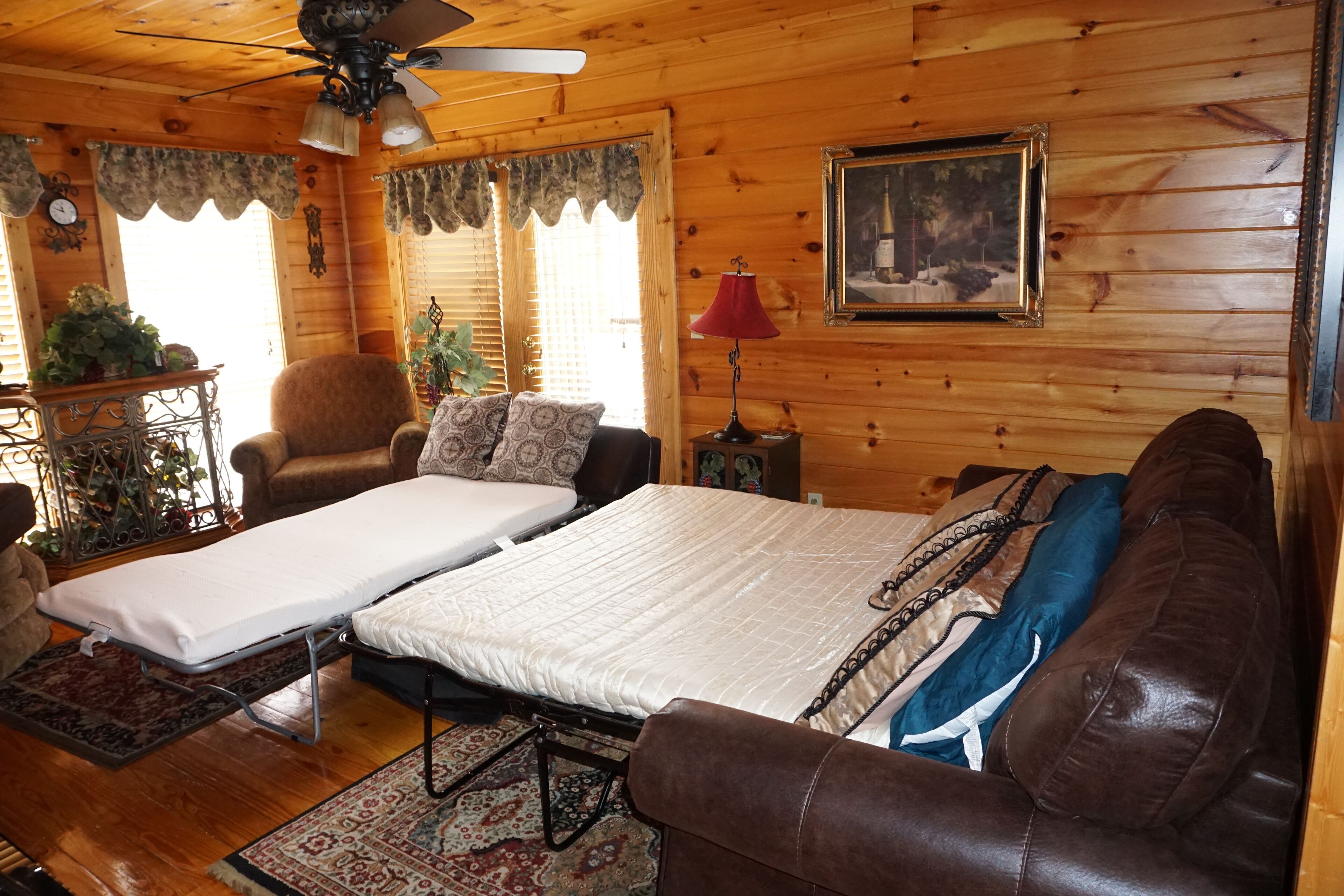 L’intérieur d’un chalet chaleureux, avec un lit, un canapé en cuir marron, un plafond en bois et un tableau accroché au mur.
