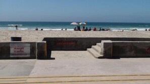 Een strand met een betonnen barrière, een bord waarop roken verboden is, en mensen die ontspannen onder parasols.