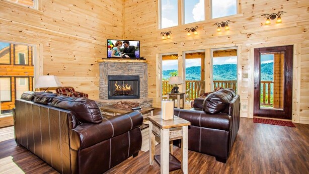 Acogedor interior de cabaña de madera con chimenea de piedra, sofás de cuero y un televisor.