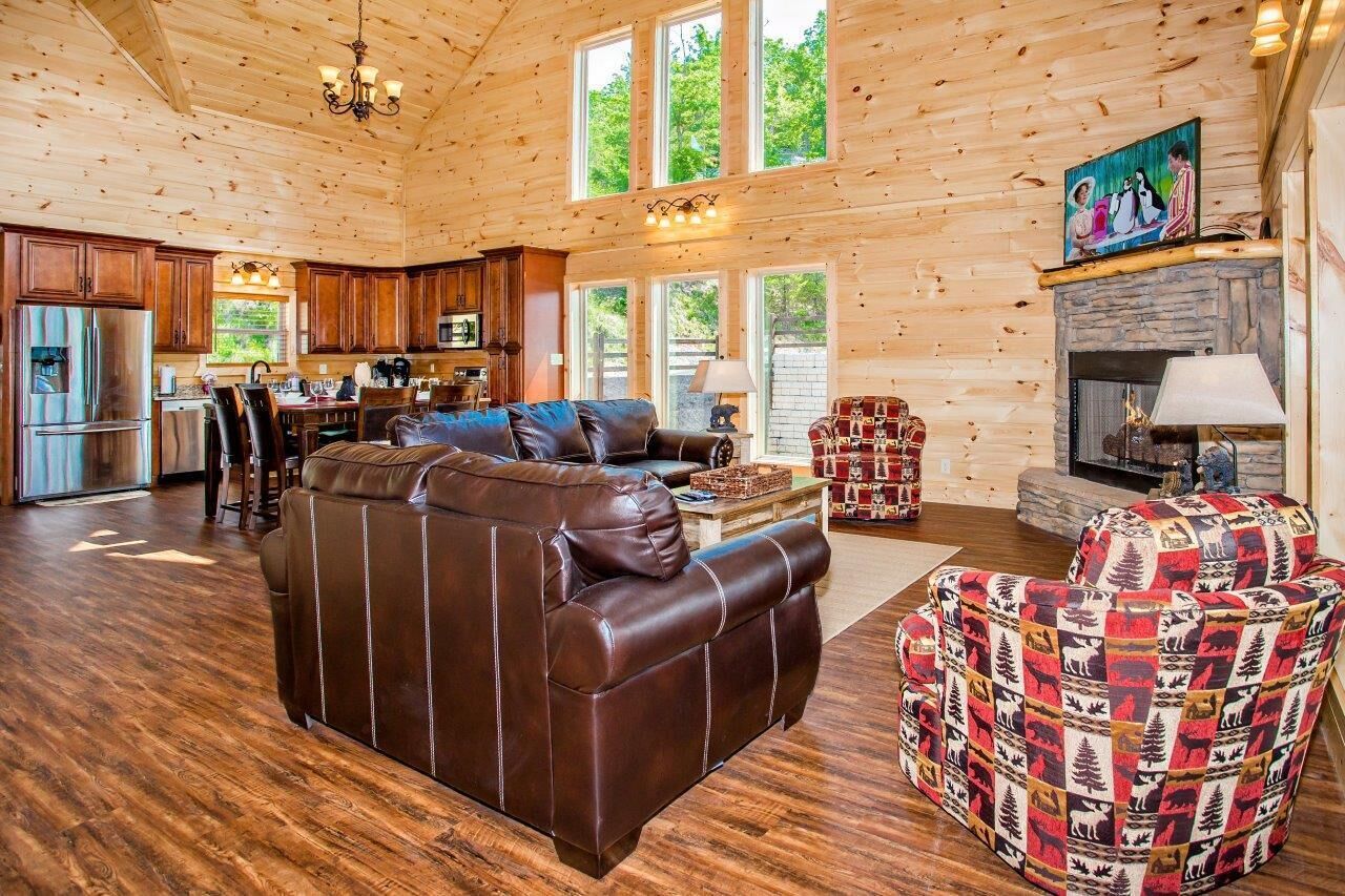 A spacious log cabin interior with a leather sofa, patterned armchair, and a fireplace.